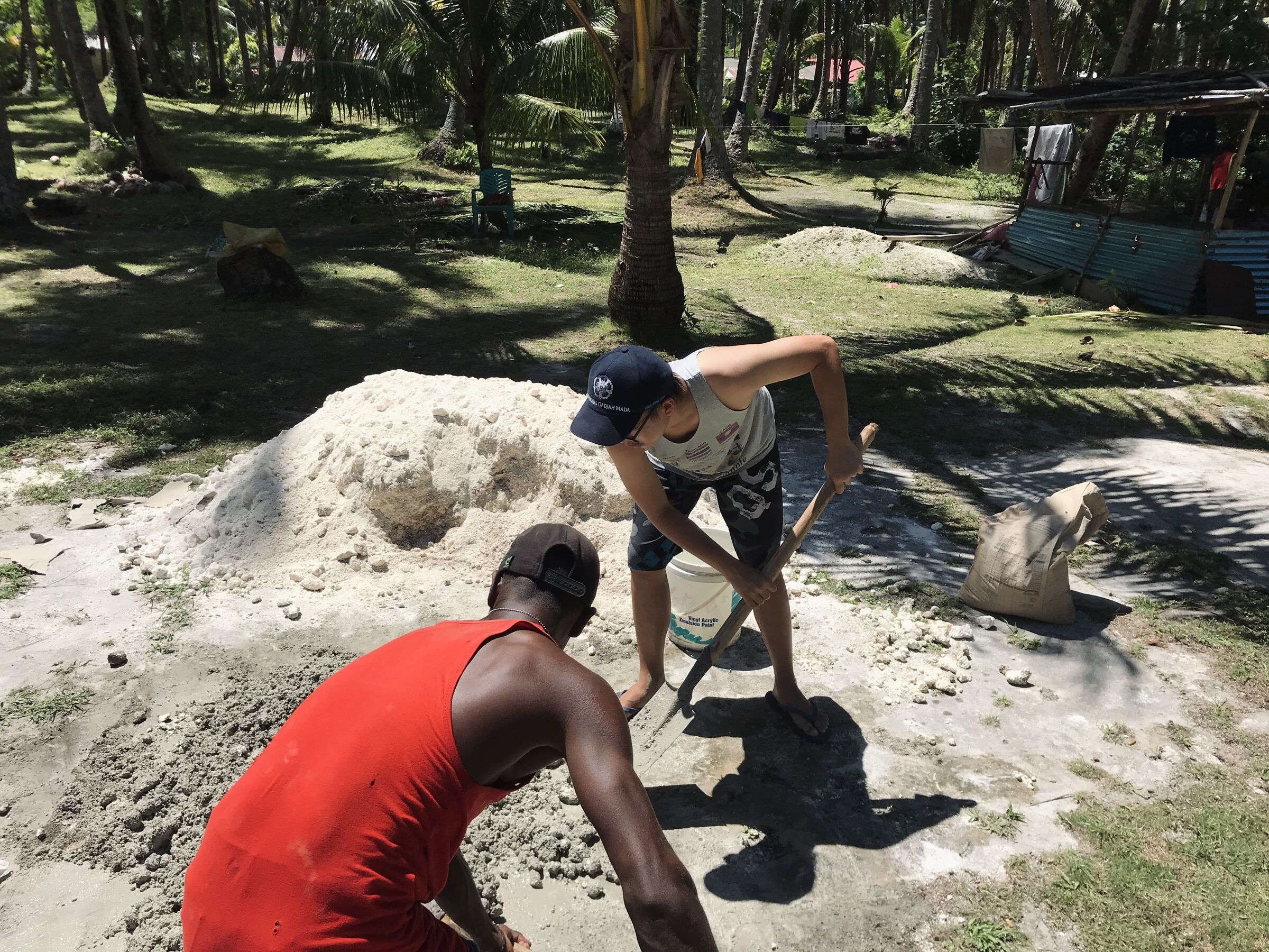 Two of us mixing concrete by hand under coconut trees