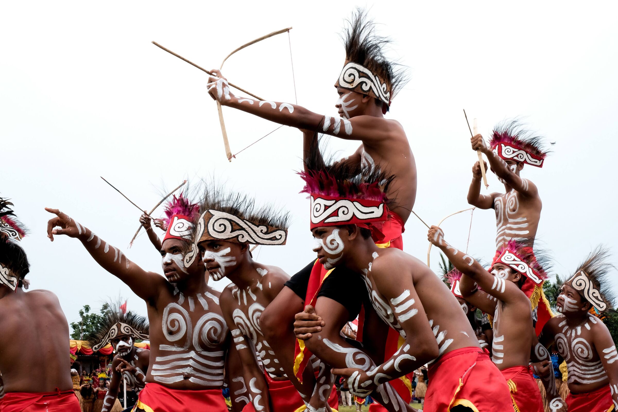 Traditional Papuan dancers in painted faces and feathered headdresses, raising bows