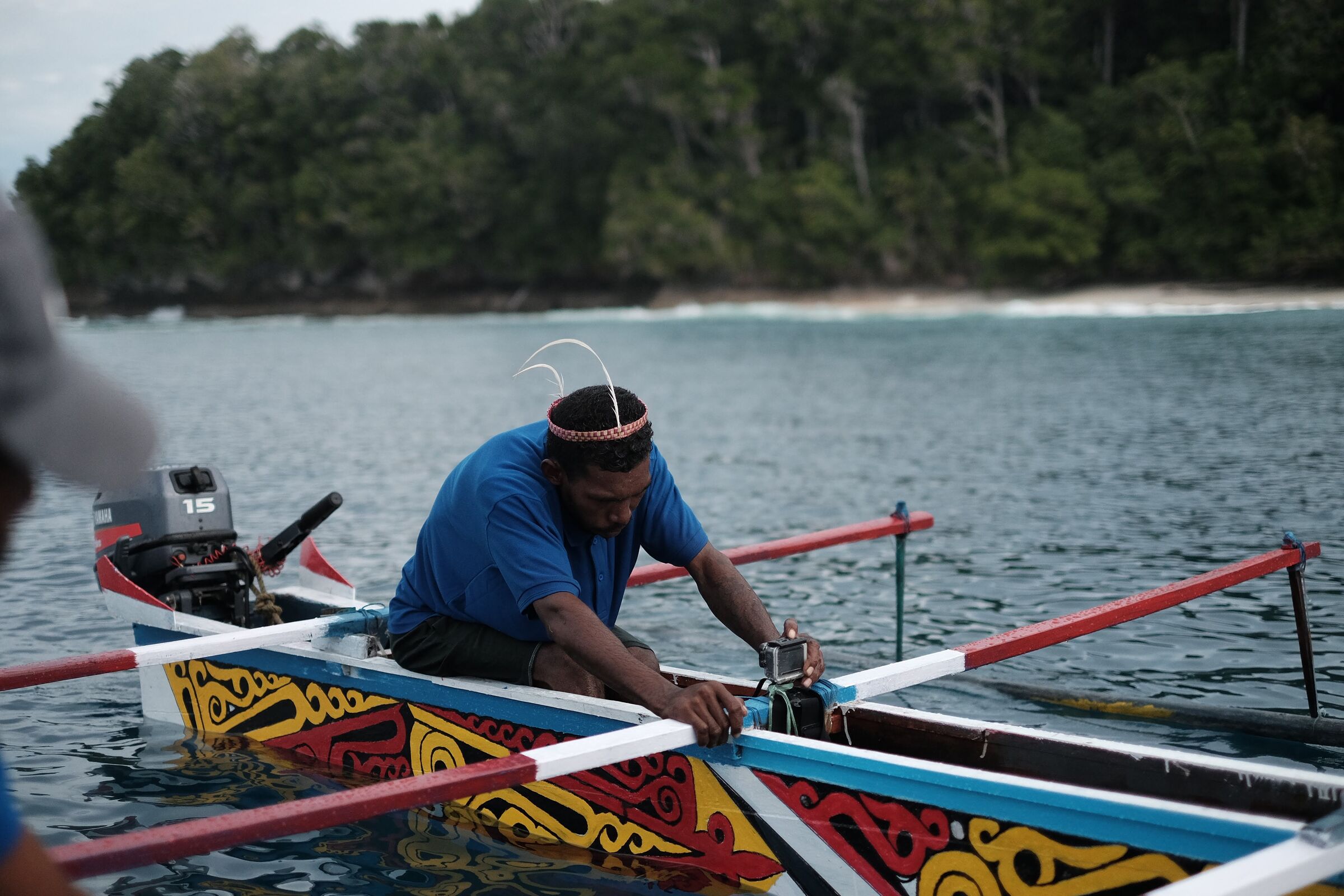 A man in a traditional headband working on a brightly painted racing boat