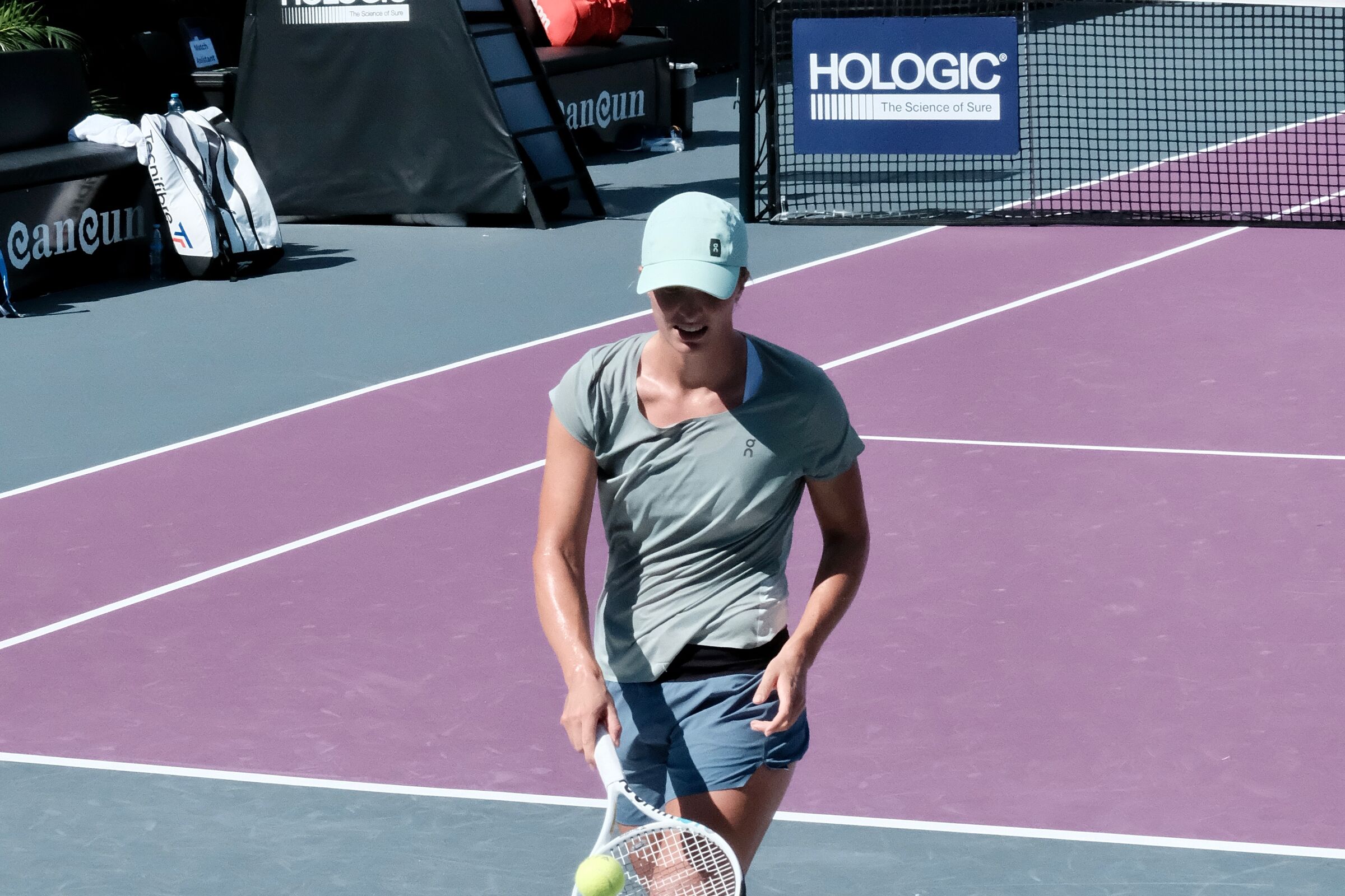 A player in a light cap and gray tee on a purple practice court, Cancun branding in the background