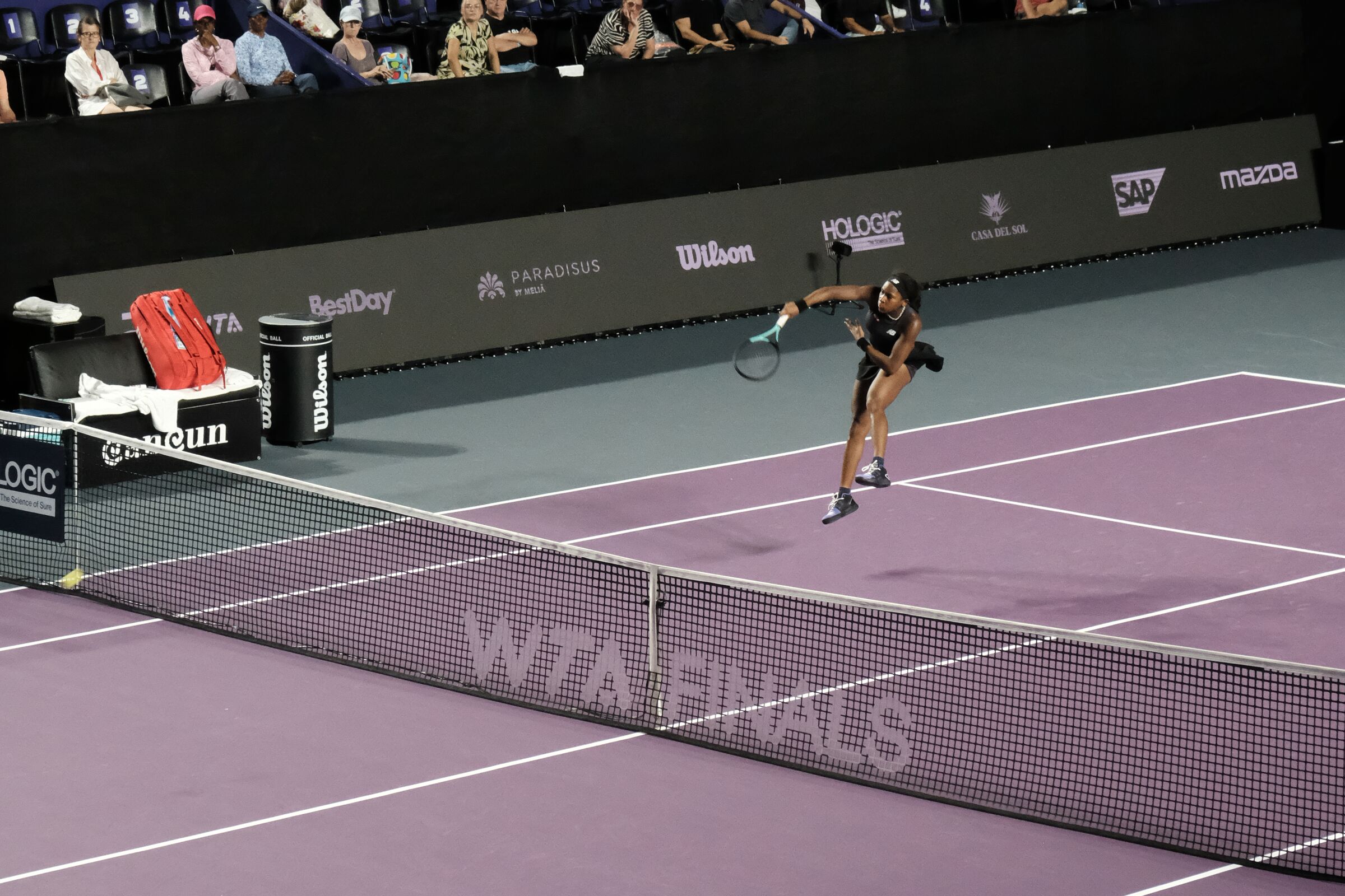 A player serving, sponsor walls behind, crowd visible at the top of frame