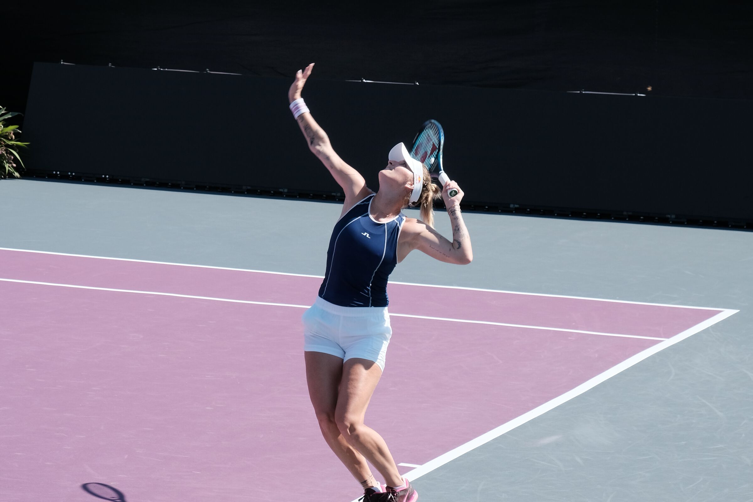 A player mid-serve on an outdoor practice court in bright sunlight