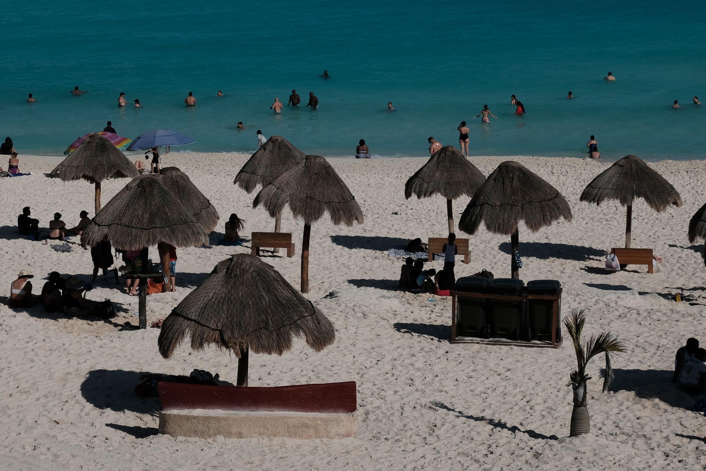 Cancun beach with thatched palapas, swimmers, turquoise water, and pale sand