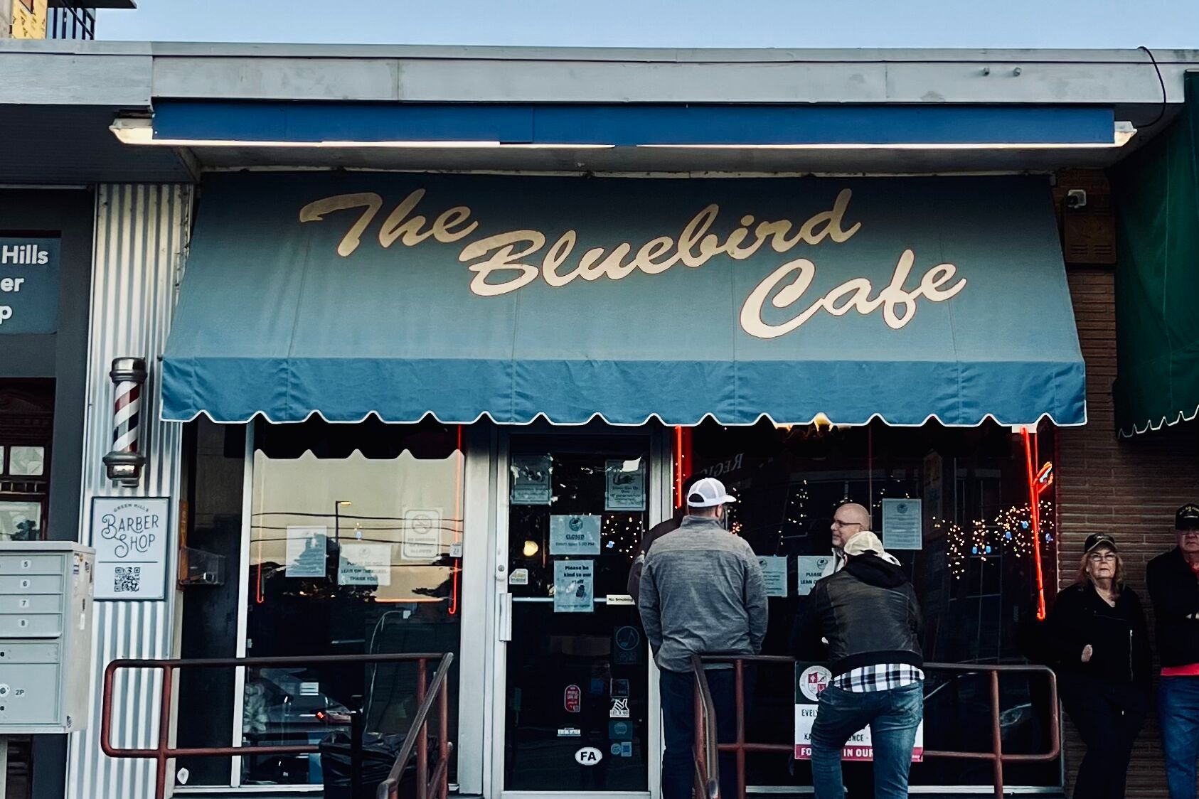 The Bluebird Cafe storefront with its blue and yellow awning, two people waiting at the door