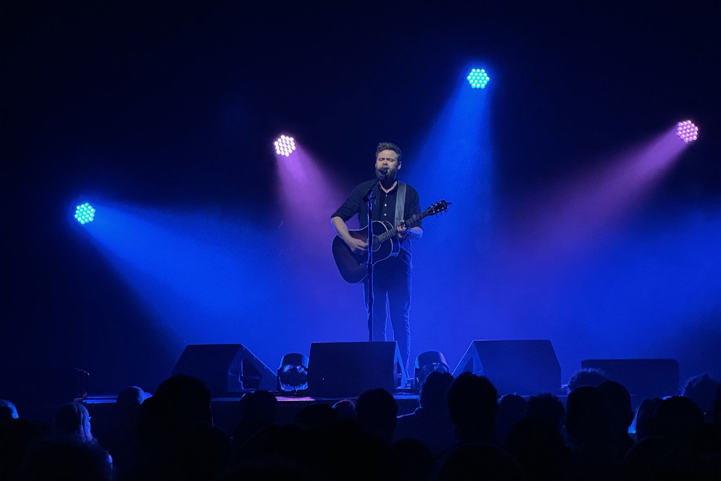 Passenger on stage at the Ryman Auditorium under blue stage lights, audience silhouettes in the foreground