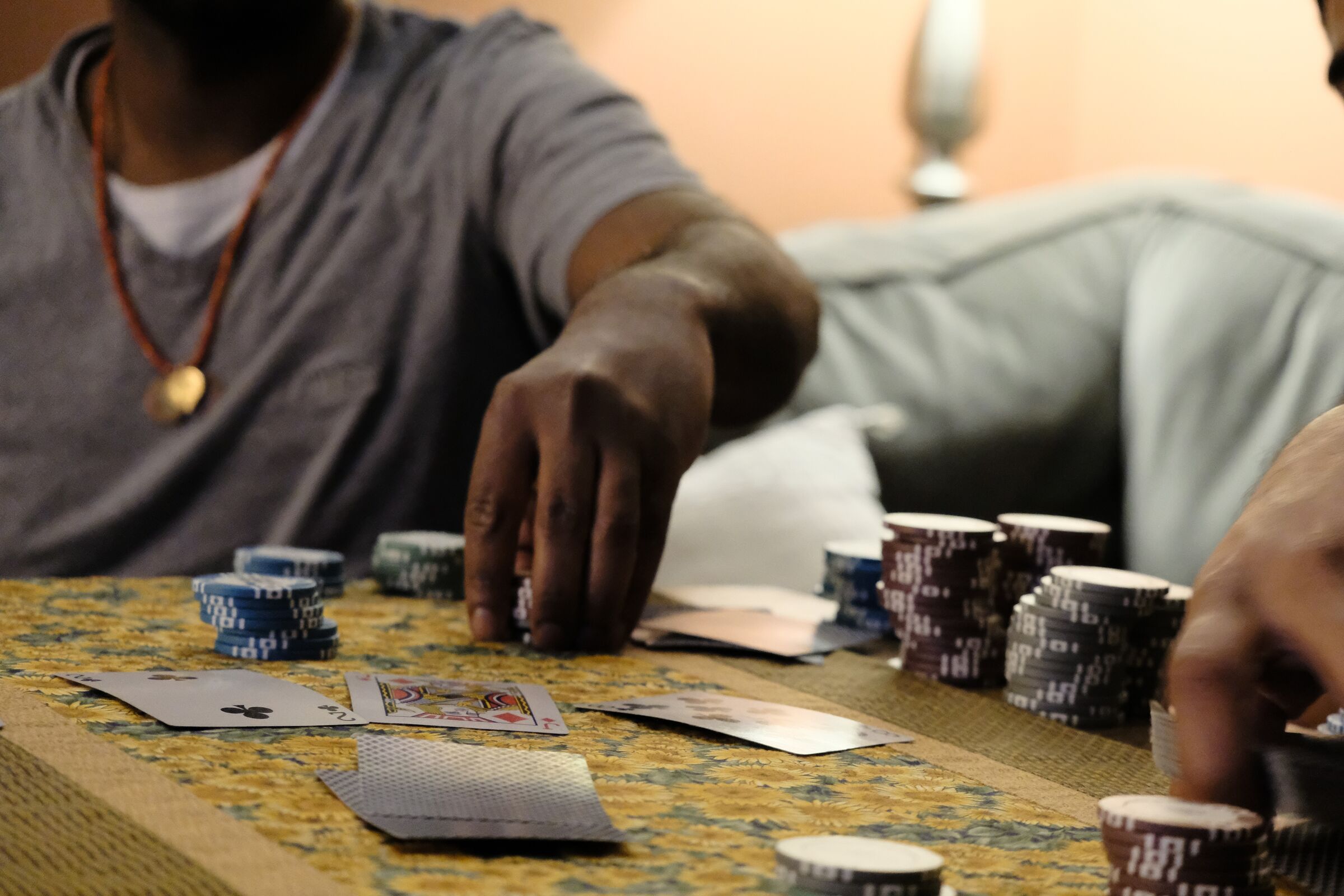 Close-up of a poker game in progress: a player's hand reaching for chip stacks on a patterned table, cards face-up