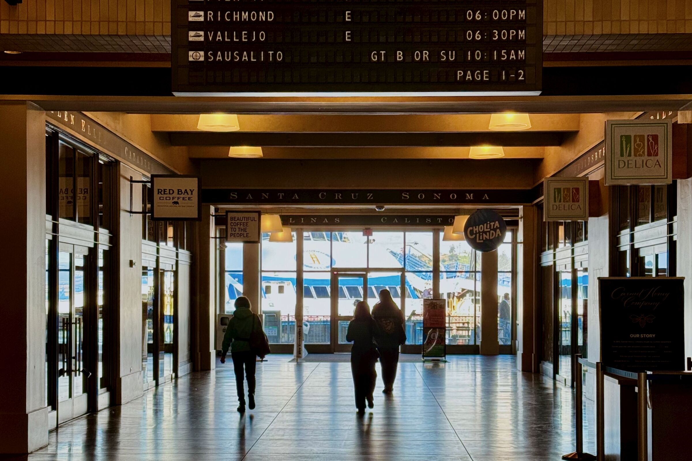 Inside the Ferry Building looking toward the gates with a departures board listing Sausalito above
