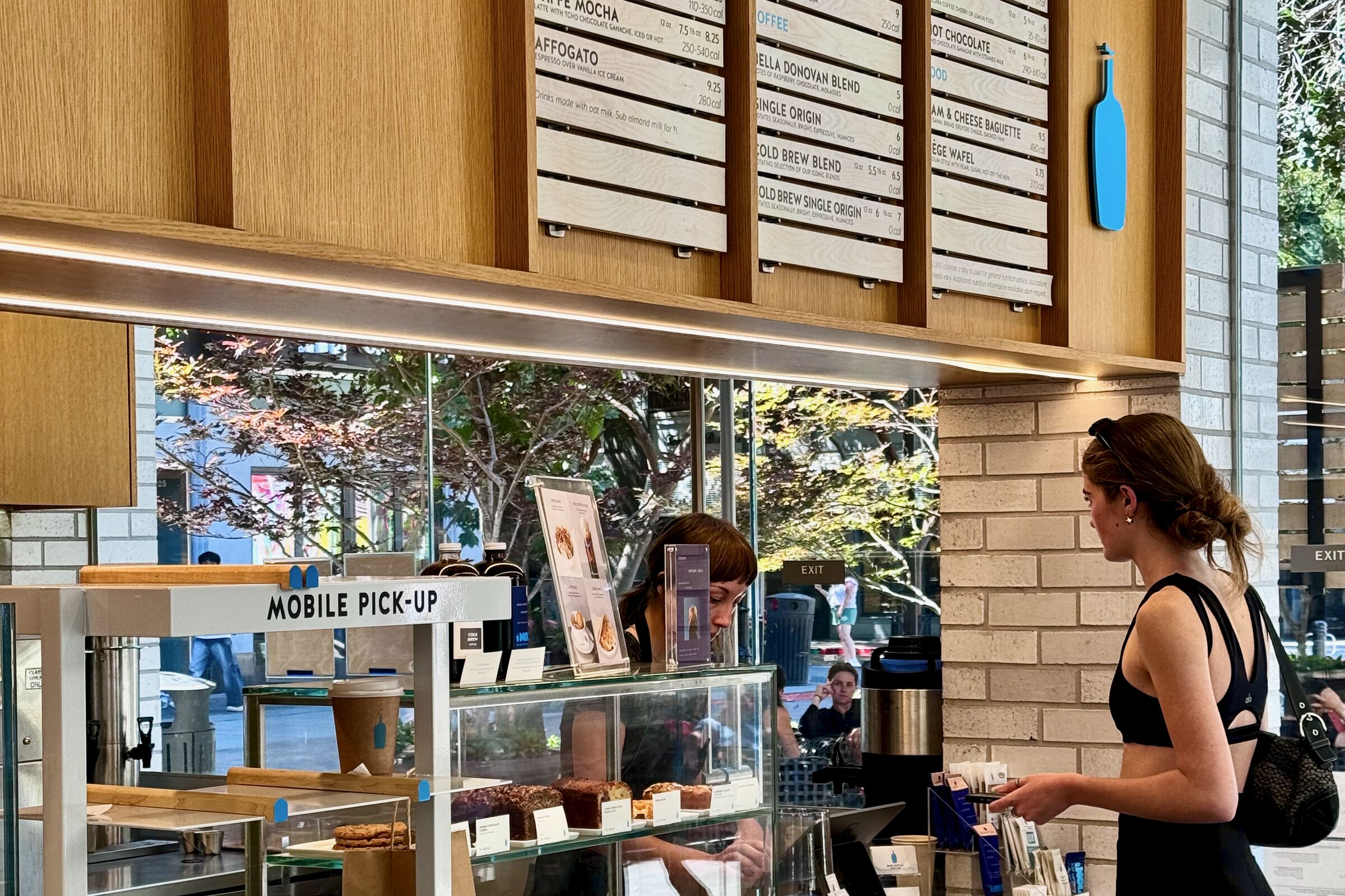 Blue Bottle Coffee counter with menu boards above and a customer in line